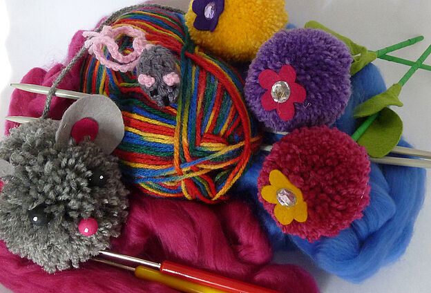Foto Wollzauber Feierwerk Dschungelpalast. Zu sehen ist ein Wollknäuel und Woll-Pompons.