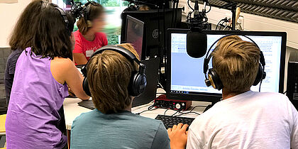 Foto Podcast-Lab in der Feierwerk Funkstation. Zu sehen sind fünf Kinder, die um Computerbildschirme und Mikros sitzen.
