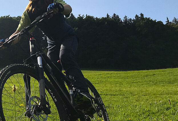 Foto Mountainbike Fahrtechniktraining mit Feierwerk Boom. Zu sehen ist eine Wiese, auf dem ein Mountainbike fährt.