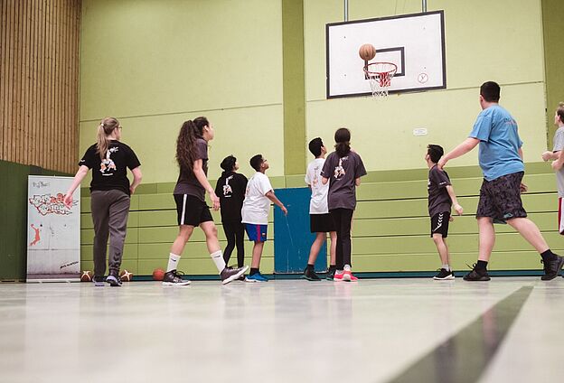 Kinder und Jugendliche spielen in einer Halle Basketball