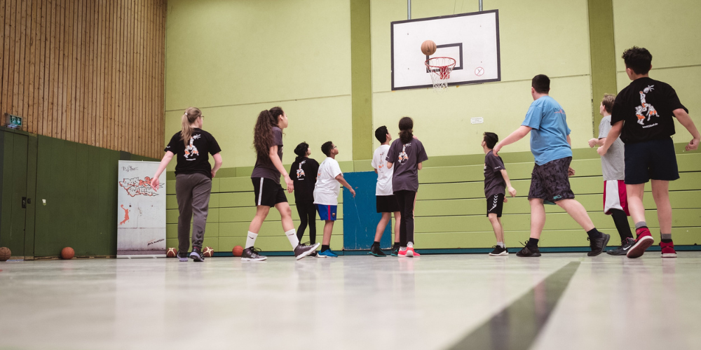 Kinder und Jugendliche spielen in einer Halle Basketball